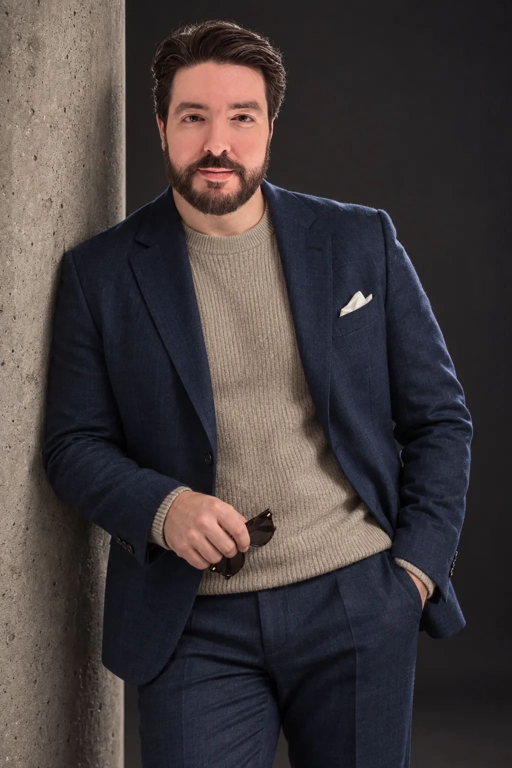 Nick DiMoro in a navy jacket and oatmeal knit sweater, leaning on a concrete column